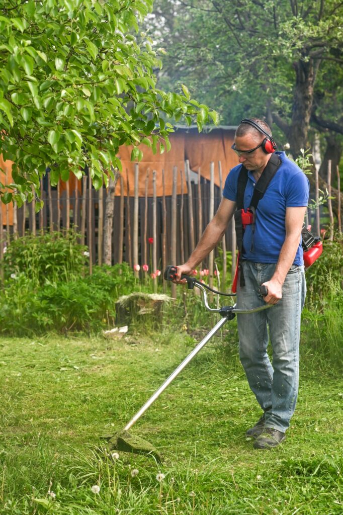 A worker mows the grass on the lawn in the garden with a handheld lawn mower.