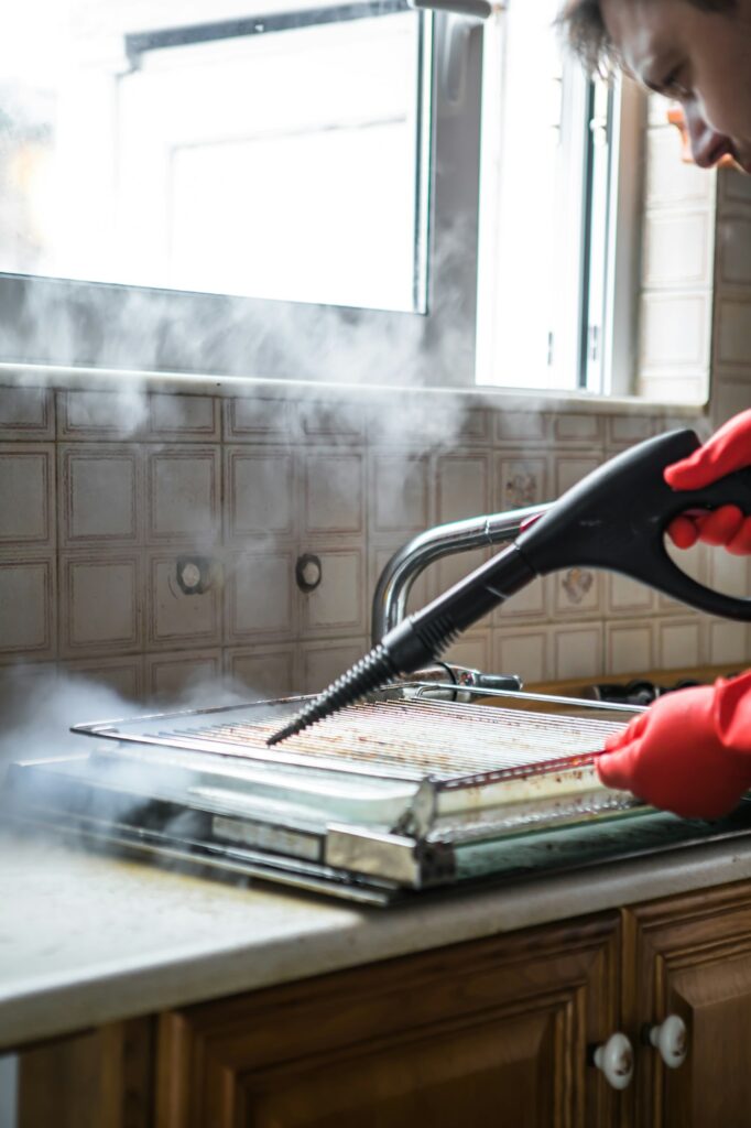 Gloved cleaner washing oven with steamer at home closeup