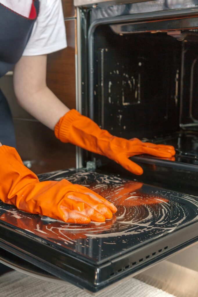 Kitchen cleaning. Girl's hands in gloves wash clean the stove, kitchen oven in the kitchen